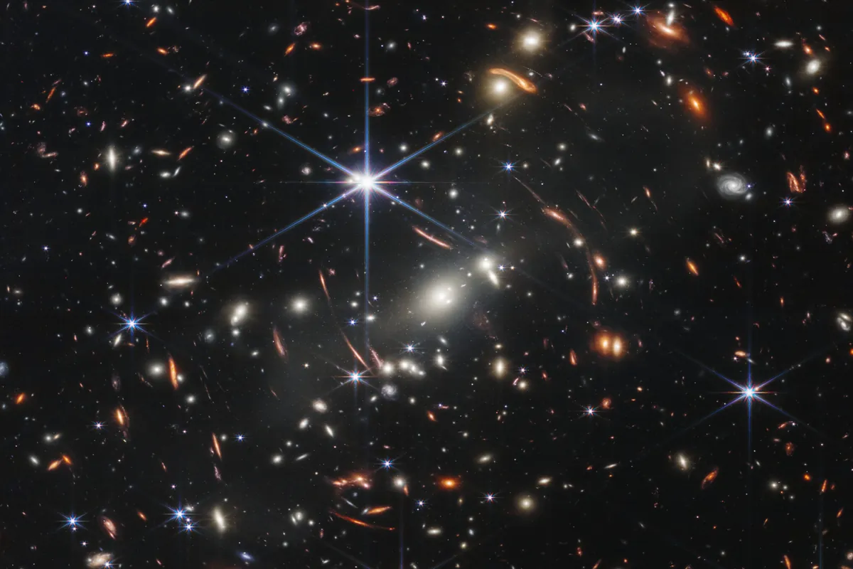 Webb image of the galaxy cluster SMACS 0723, crowded with galaxies of many sizes and arcs of lensed galaxies around the foreground cluster