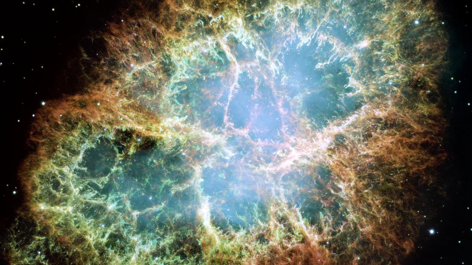 Hubble image of the Crab Nebula, orange and yellow filaments of gas wrapped around a bluish-white interior